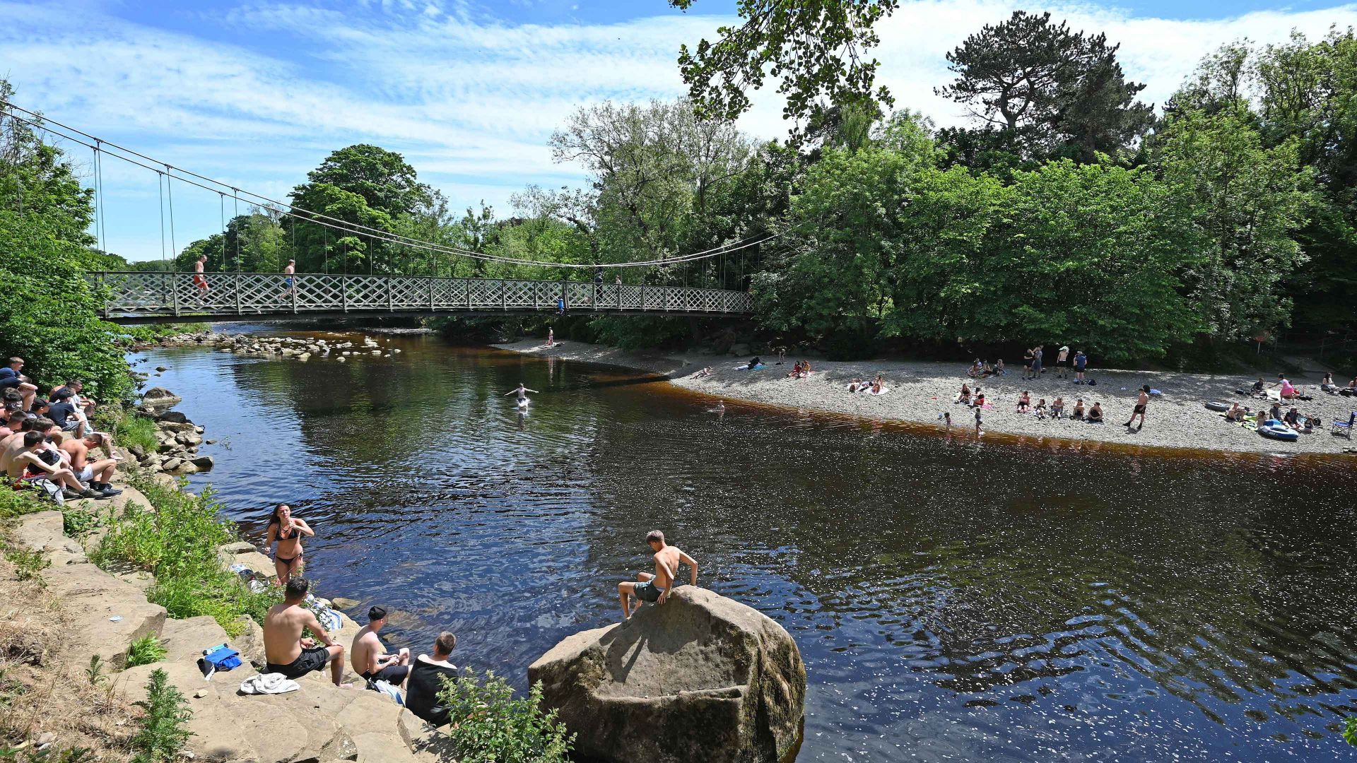 A woman jumps from the suspension bridge into the water as others relax on the banks of the River Wharfe in Ilkley. Photo: PAUL ELLIS/AFP via Getty Images