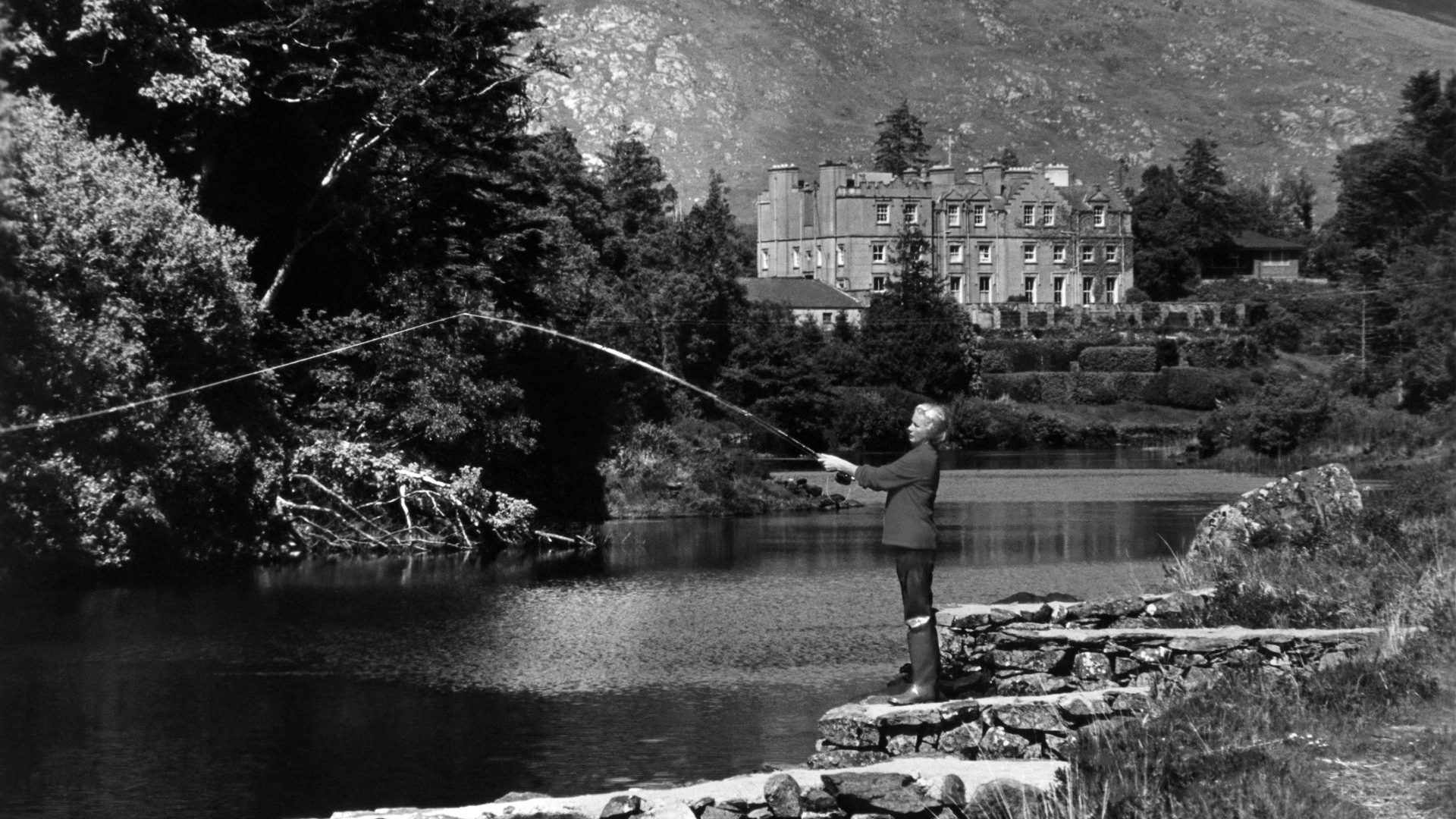 A woman stands fishing on the bank of the Ballynahinch River in Ireland with mountains in the background in 1970. Photo: International Game Fish Association via Getty Images